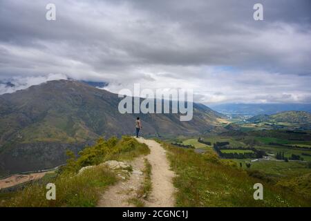 Ein Mann steht auf einem Hügel, um im Sommer in Otago, Neuseeland, einen Panoramablick auf den Arrow Junction Lookout Point zu genießen. Stockfoto