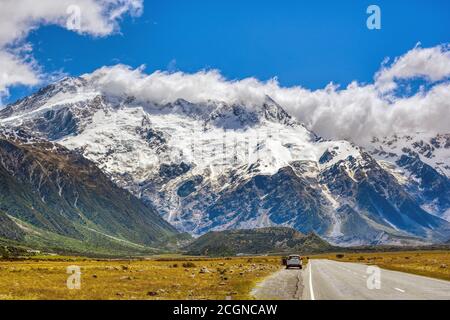 Eine gerade Straße führt zu einem großen Berg gibt es Autos am Straßenrand geparkt. Spektakuläre Aussicht auf die Berge in der Sommersaison am Mount Cook Nation Stockfoto