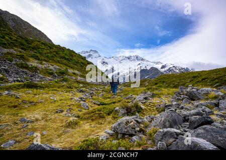 Zwei Touristen laufen zum Kea Point Track im Mount Cook Nationalpark, hohe felsige Berge und grünes Gras im Sommer in Neuseeland. Stockfoto