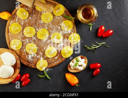 Leckere Ravioli mit Mehl, Kirschtomaten, Sonnenblumenöl und Basilikum auf dunklem Grund. Der Prozess der Herstellung von italienischen Ravioli. Speicherplatz kopieren. Flach l Stockfoto