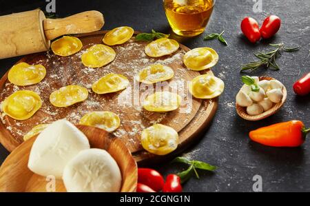 Leckere Ravioli mit Mehl, Kirschtomaten, Sonnenblumenöl und Basilikum auf dunklem Grund. Der Prozess der Herstellung von italienischen Ravioli. Seitenansicht. Stockfoto