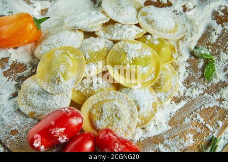 Leckere Ravioli mit Mehl, Kirschtomaten, Sonnenblumenöl und Basilikum auf dunklem Grund. Der Prozess der Herstellung von italienischen Ravioli. Nahaufnahme Stockfoto