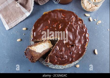Käsekuchen Snickers mit Schokolade, Karamell, Erdnusspaste, Nougat und Erdnusskuchen auf blauem Beton-Tischhintergrund. Draufsicht Stockfoto