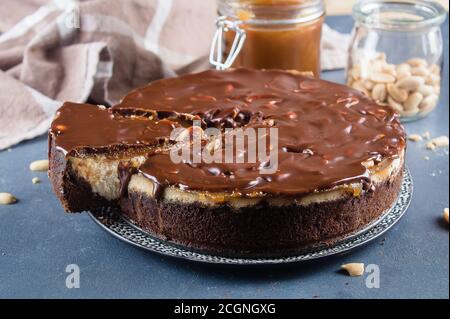 Käsekuchen Snickers mit Schokolade, Karamell, Erdnusspaste, Nougat und Erdnusskuchen auf blauem Beton-Tischhintergrund. Stockfoto