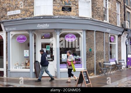 Business as usual Konzept - ein weiblicher und männlicher Spaziergang vorbei Smiths The Bakers Store in der High Street, Kings Lynn, Norfolk, Großbritannien Stockfoto