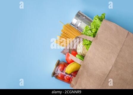 Papiertüte mit Lebensmitteln, Konserven, Tomaten, Gurken, Bananen auf gelbem Hintergrund. Spende, Quarantäne des Coronavirus. Lebensmittel für Quarantäne. Stockfoto