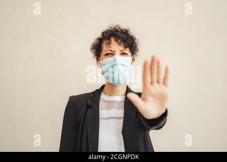 Portrait der kaukasischen Unternehmerin trägt Gesichtsmaske und zeigt Stop-Geste während Covid-19 Ausbruch Stockfoto