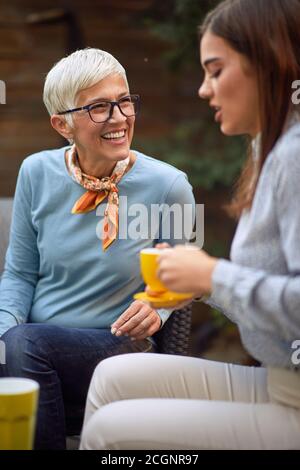 Alte fröhliche Mutter und junge Erwachsene Tochter reden, trinken Kaffee Stockfoto