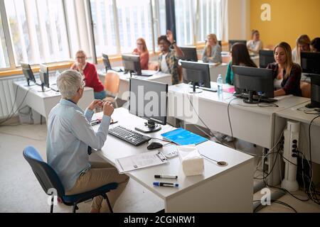 Ein männlicher Schüler, der bei einem Vortrag die Hand für Fragen erhebt Im Uni-Computer-Calssroom Stockfoto