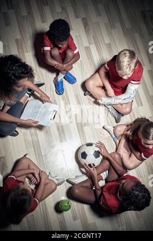 Kid's Fußball-Team und ihre Trainerin in einem entspannten Atmosphäre, die über Training spricht Stockfoto