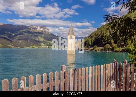 Terrasse, umgeben von einem Holzzaun mit dem Glockenturm im Hintergrund, der aus dem Reschensee, Südtirol, Italien, hervorgeht Stockfoto
