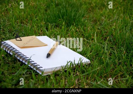 Konzept der Nachhaltigkeit mit Notizbuch und Stift aus recycelbaren Materialien und einer Notiz mit dem Wort Sustainable darauf geschrieben. Buch auf dem Rasen Stockfoto