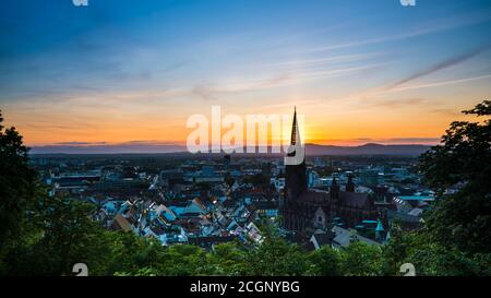 Deutschland, Freiburg im Breisgau, schöner orangefarbener Sonnenuntergang hinter dem Kirchturm des berühmten Münsters, Luftaufnahme von oben Stockfoto