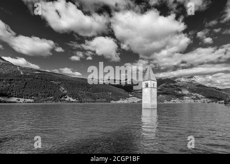 Schöne Schwarz-Weiß-Ansicht des alten Glockenturms des Graun Vinschgau, der aus dem Reschensee, Südtirol, Italien, gegen einen dramatischen Himmel auftaucht Stockfoto
