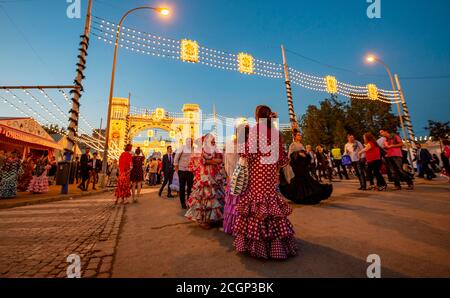 Spanische Frauen mit Flamenco-Kleidern vor der beleuchteten Portada, Eingangstor, Feria de Abril, Sevilla, Andalusien, Spanien Stockfoto