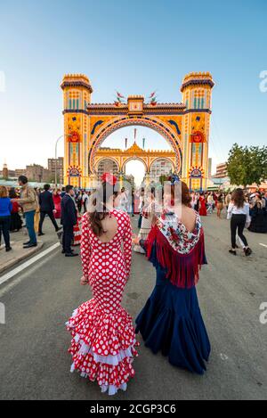 Spanische Frauen mit Flamenco-Kleidern vor der beleuchteten Portada, Eingangstor, Feria de Abril, Sevilla, Andalusien, Spanien Stockfoto