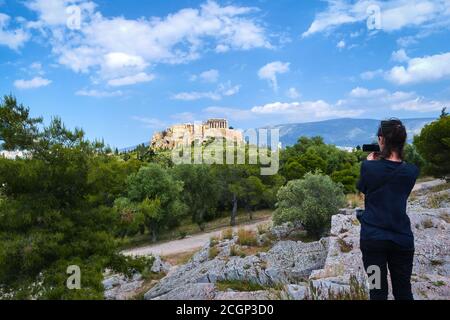 Unkenntlich weibliche Touristen in schwarz gekleidet schießt einen Blick Akropolis und Lycabettus Hügel in Athen, Griechenland von Pnyx Hügel an sonnigen Sommertag Stockfoto