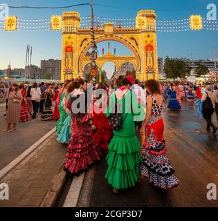 Spanische Frauen mit Flamenco-Kleidern vor der beleuchteten Portada, Eingangstor, Feria de Abril, Sevilla, Andalusien, Spanien Stockfoto