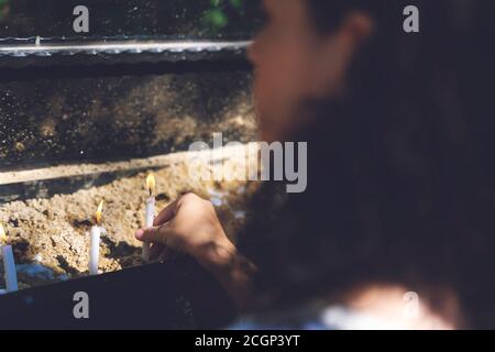 Frau, die im Garten des Hauses der Jungfrau Maria betet und Kerzen brennt. Brennende weiße Kerzen auf dem Stand. Anbetung Stockfoto