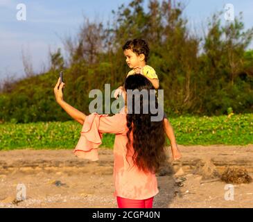 Eine asiatische Mutter setzte ihr Kind auf ihre Schulter und Ich habe ein Selfie mit einer Smartphone-Kamera gemacht Stockfoto