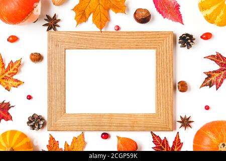Unbeschriftete Fotokarte im Rahmen aus Herbstblättern, Kürbissen, Nüssen und Beeren auf weißem Hintergrund. Nachbildung. Flach liegend. Herbst oder Thanksgiving com Stockfoto