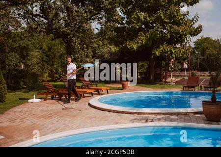 Ein kaukasischer Gärtner mit einem Netz für die Reinigung des Pools Neben dem Pool in der Natur Stockfoto