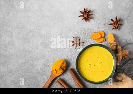 Traditionelles indisches Getränk Kurkuma Latte oder goldene Milch mit Zimt, Ingwer, Anis, Pfeffer auf betontem Hintergrund. Gesundes Herbst- oder Wintergetränk Stockfoto