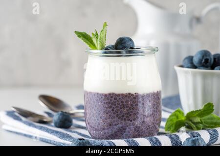 Heidelbeer-Joghurt-Parfait mit Chia-Pudding, Kokosjoghurt, frischen Beeren und Minze im Glas für gesundes Diätfrühstück auf Serviette über Marmortisch Stockfoto