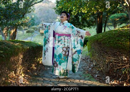 Schöner japanischer Teenager mit traditionellem Kimono, der mit ausgestreckten Armen aufschaut und das Kommen des Age Day anpreist, dankt und feiert. Stockfoto