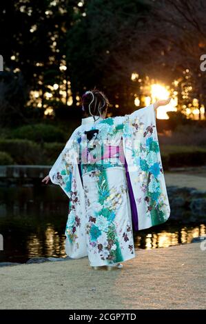 Japanischer Teenager trägt traditionellen Kimono Rücken und Arme ausgestreckt mit schönen Sonnenschein und Flare feiert den kommenden Age Day. Stockfoto