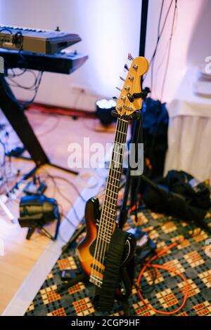 Gitarre auf einem Gitarrenständer im Raum eines Musikers mit Keyboard und LED-Köpfen im Hintergrund. Stockfoto