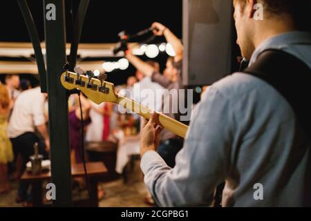 Ein Mann spielt Gitarre bei einem Konzert auf einem verschwommenen Hintergrund des Tanzens. Rückansicht, der Gitarrist fingern den Hals der Gitarre. Stockfoto