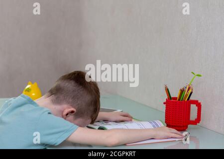 Müde traurige junge zu Hause studieren online während der Quarantäne. ired traurigen Jungen zu Hause studieren online. Schlafen Sie am Schreibtisch ein, während Sie Hausaufgaben machen. Stockfoto
