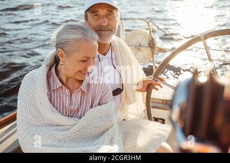 Ein paar von zwei reifen Menschen in Kart auf einem Segelboot eingewickelt. Senior Mann in Kappe Lenkung einer Yacht. Stockfoto