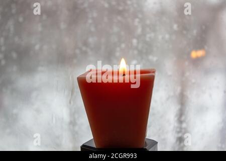 Kerze brennt in der Nähe eines Milchfensters in der Dämmerung. Winterabend Stockfoto