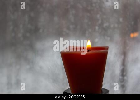 Kerze brennt in der Nähe eines Milchfensters in der Dämmerung. Winterabend Stockfoto