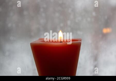 Kerze brennt in der Nähe eines Milchfensters in der Dämmerung. Winterabend Stockfoto