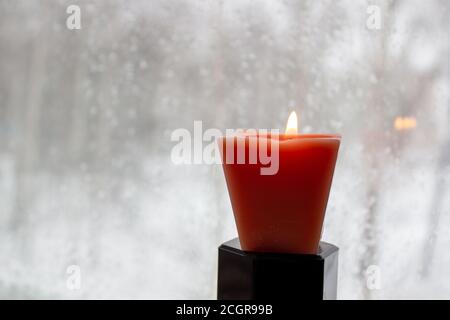 Kerze brennt in der Nähe eines Milchfensters in der Dämmerung. Winterabend Stockfoto