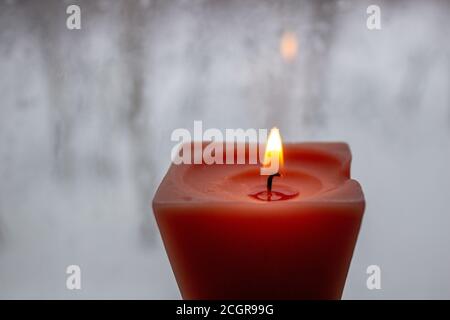 Kerze brennt in der Nähe eines Milchfensters in der Dämmerung. Winterabend Stockfoto