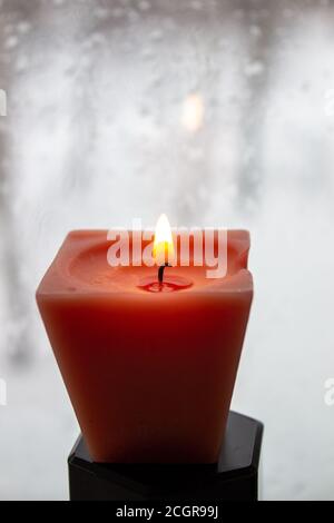 Kerze brennt in der Nähe eines Milchfensters in der Dämmerung. Winterabend Stockfoto