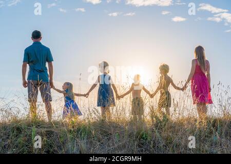 Eine große Familie steht mit Händen vor dem Hintergrund des Sonnenuntergangs. Stockfoto