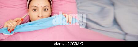 Portrait junge Frau mit Windpocken im Bett liegen und messen Temperatur Stockfoto