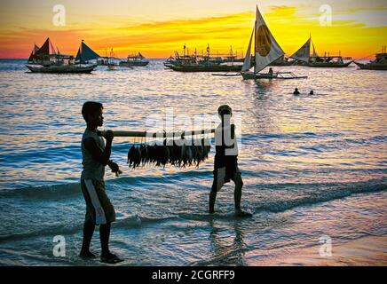 Die Silhouette von vier Segelbooten bei Sonnenuntergang entlang des White Beach auf Boracay Island, Aklan, Philippinen. Der Himmel sieht gelb orange aus wie ein Feuerball. Stockfoto