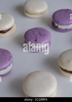 Violette und weiße Mandel- und Meringue-Makronen auf einem weißen Tisch mit weißer und dunkler Schokolade Dulce de leche Maus und Schlagsahne gekrönt. Stockfoto