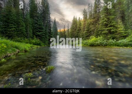 Blick auf den Lostine River im Wald mit Berggipfeln im Hintergrund in Oregon bei Sonnenaufgang. Stockfoto