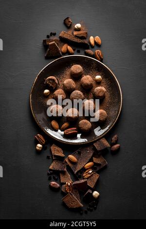Schokoladentrüffel mit dunkler Schokolade und Nüssen auf schwarzem Hintergrund, Draufsicht, Kopierraum. Vegane hausgemachte Schokolade Energie Bälle oder Trüffel für desse Stockfoto