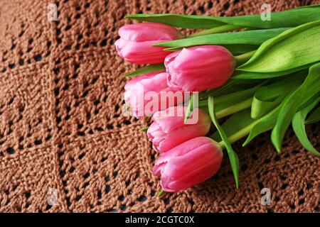 Hintergrund mit Blumen. Ein Blumenstrauß aus Tulpen, der auf einem braun gestrickten Damentuch liegt. Stockfoto