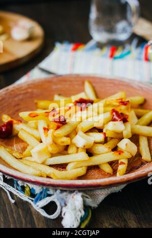 Pommes frites auf schwarzer Oberfläche anprittieren. Kanadisches Gericht mit Kartoffeln, Käse und Sauce Stockfoto