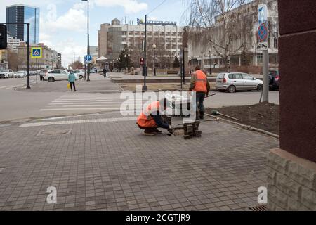 Arbeiter in hellen Schutzwesten reparieren Pflasterplatten vor einem Fußgängerübergang auf dem Hintergrund einer Stadtstraße. Stockfoto