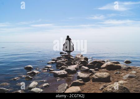 Silhouette einer Frau auf Steinen am Strand. Schöne Sommerlandschaft mit Horizont Linie. Meer und Himmel Stockfoto